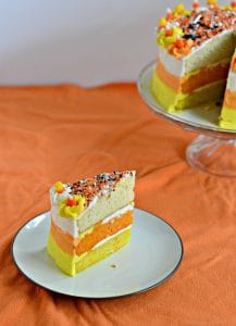 A slice of candy corn cake with the entire cake behind the slice.