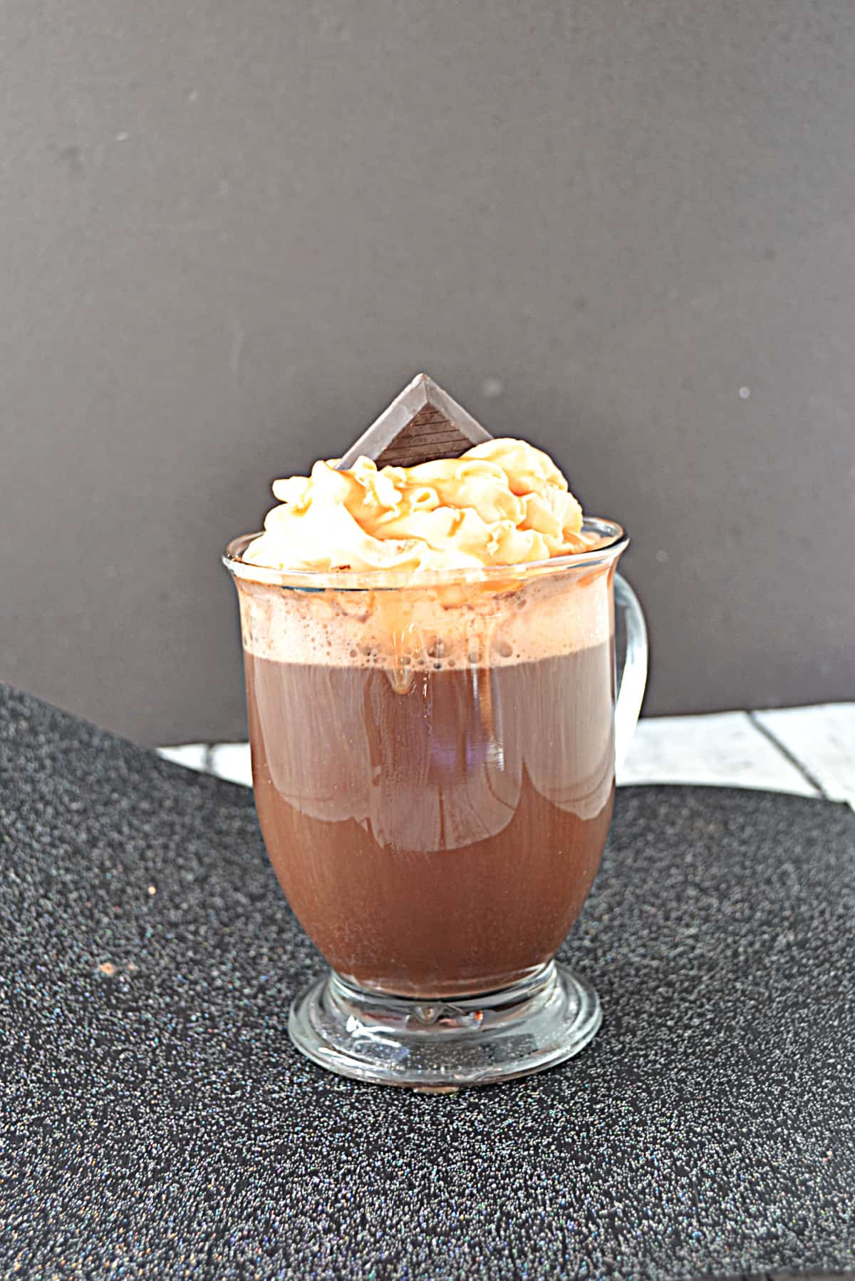 A mug of hot cocoa with whipped cream and a piece of chocolate on top.