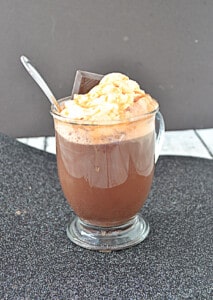 A mug of hot cocoa with a spoon in it with whipped cream on top.