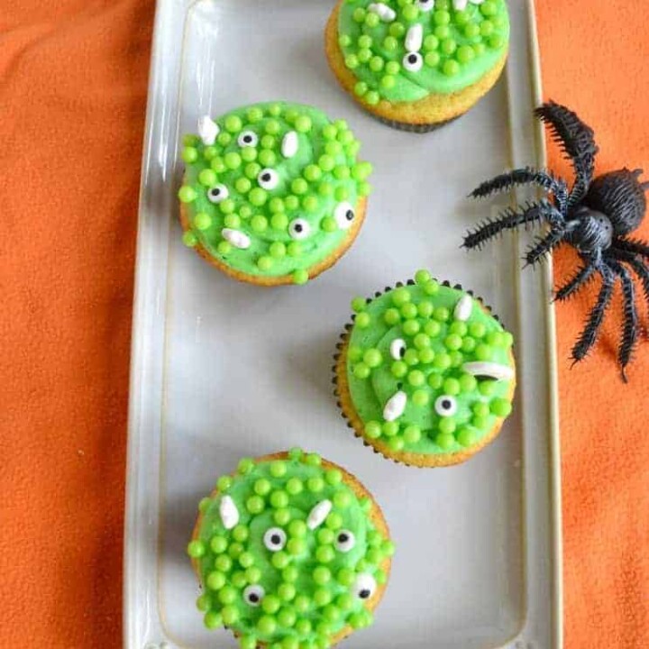 A platter with four cupcakes topped with green frosting, green bubbles, and edible eyes.