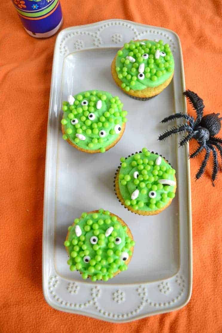 A platter with four cupcakes topped with green frosting, green bubbles, and edible eyes.