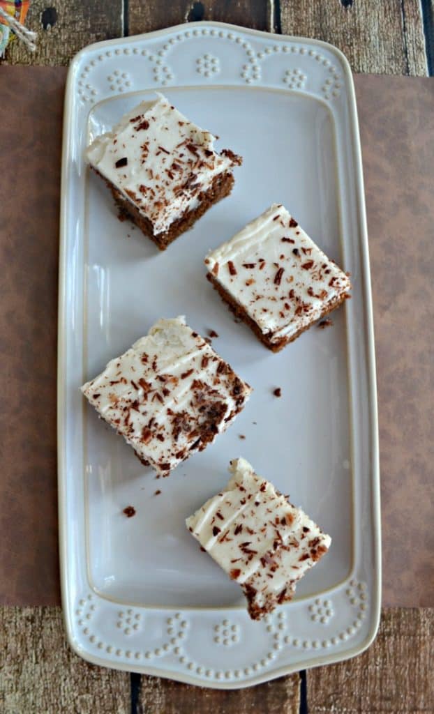 A white platter with four brownies topped with frosting and chocolate shavings. 