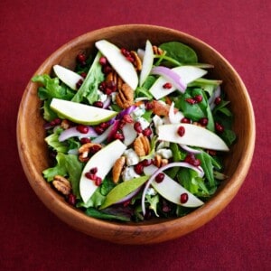 An overhead view of a bowl of salad with pears, pecans, and red onions.