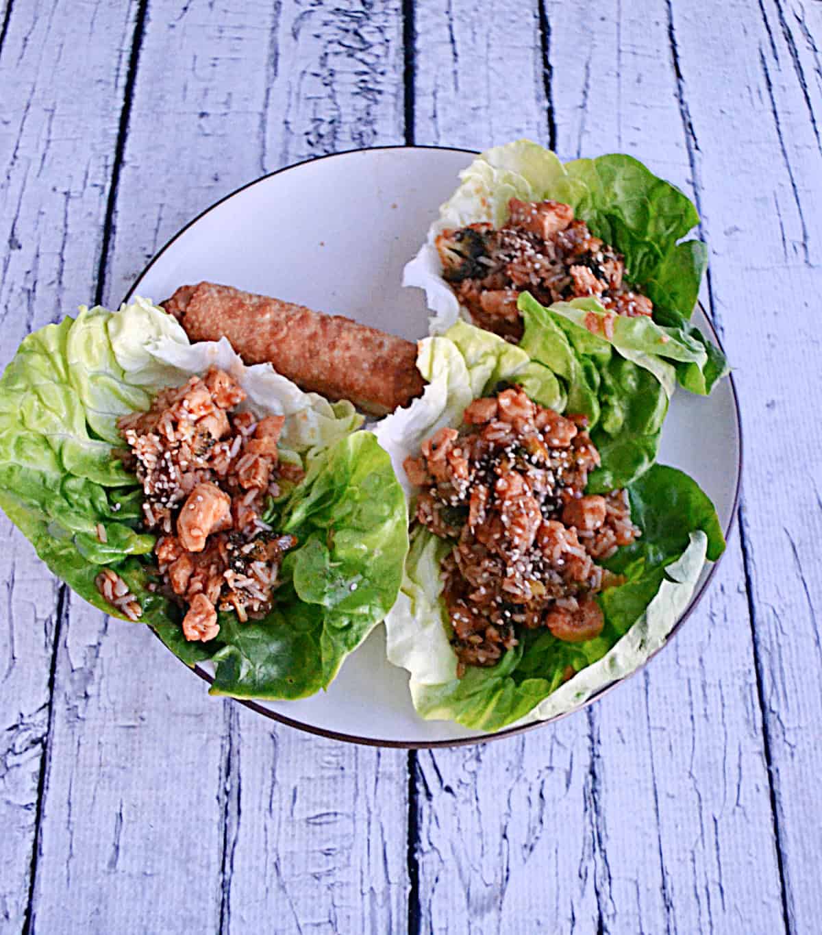 A plate with three lettuce wraps filled with chicken and rice and an egg roll on it.