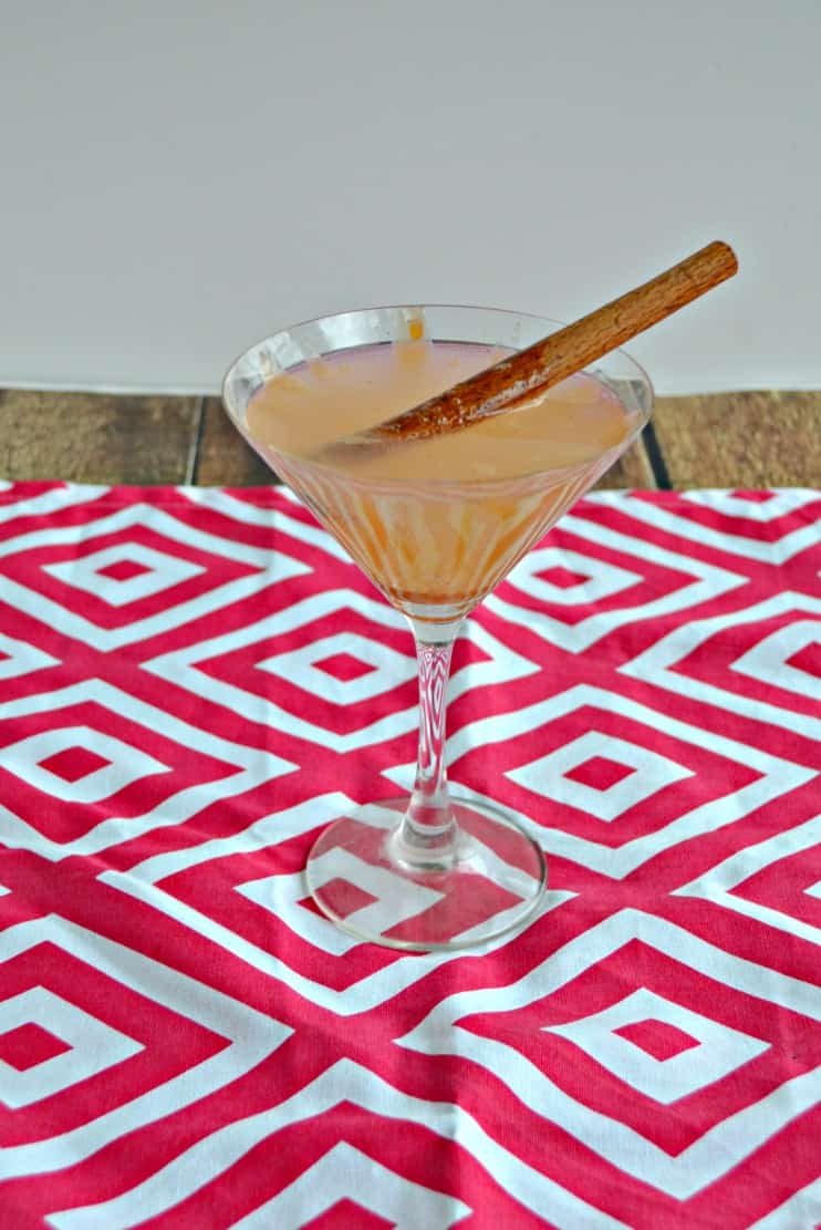 Apple martini in a glass with a cinnamon stick on a red placemat