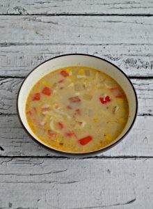 A bowl of corn and potato chowder with bits of red pepper sitting on a white wooden backdrop.