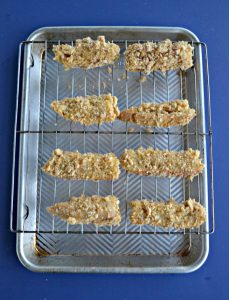 Eight french toast sticks sitting on a wire rack over top of a cookie sheet with a blue background.