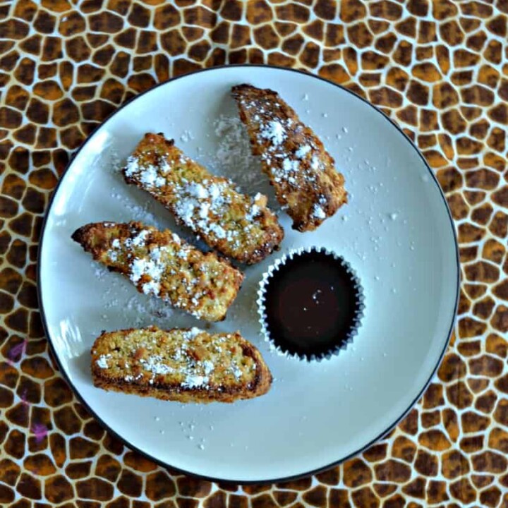 A plate with 4 French Toast sticks in a semi-circle sprinkled with powdered sugar with a cup of syrup on a cheetah background.