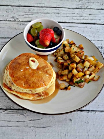 Plate with a stack of pancakes, a pile of home fries, and a small bowl of fresh fruit.