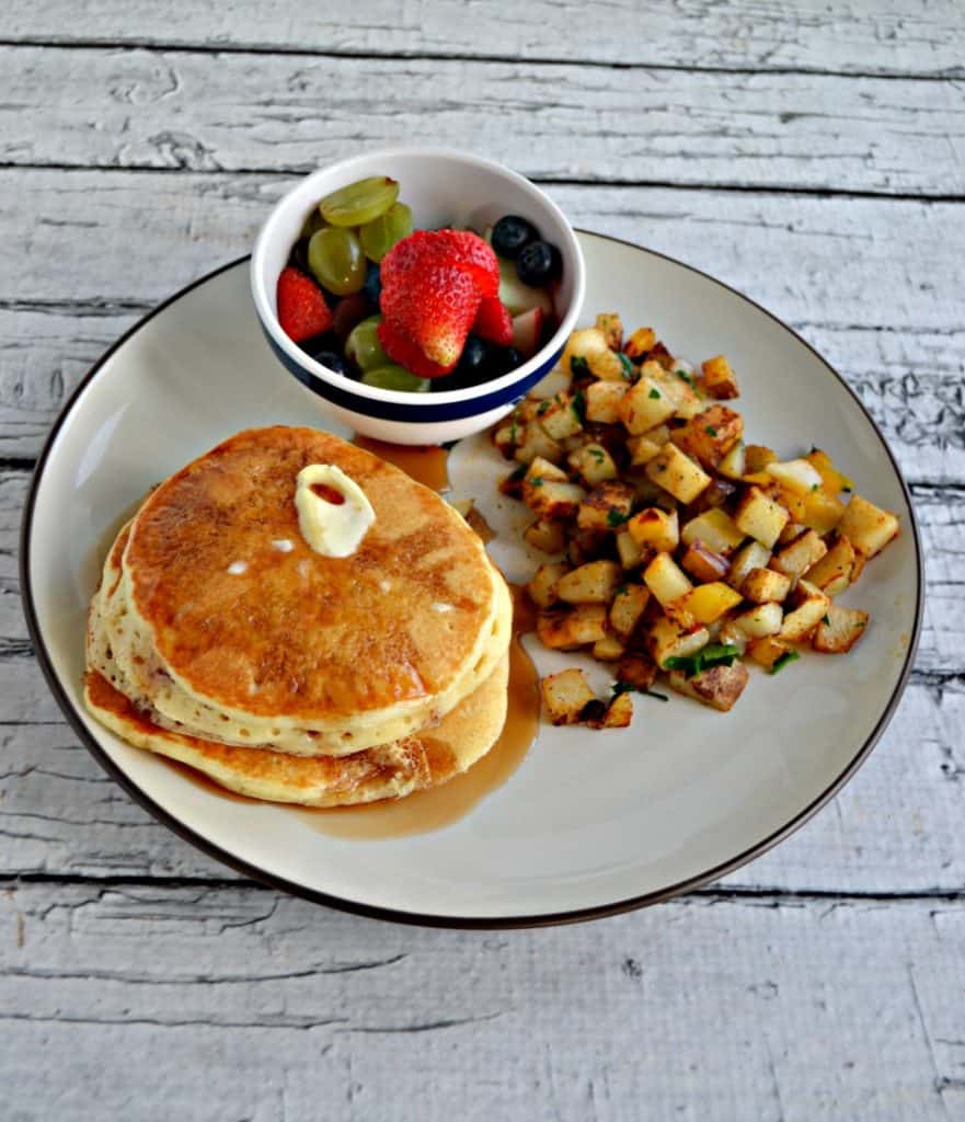 Plate with a stack of pancakes, a pile of home fries, and a small bowl of fresh fruit.