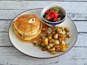 Wide angle of plate filled with a stack of pancakes, a pile of home fries, and a bowl of fruit.