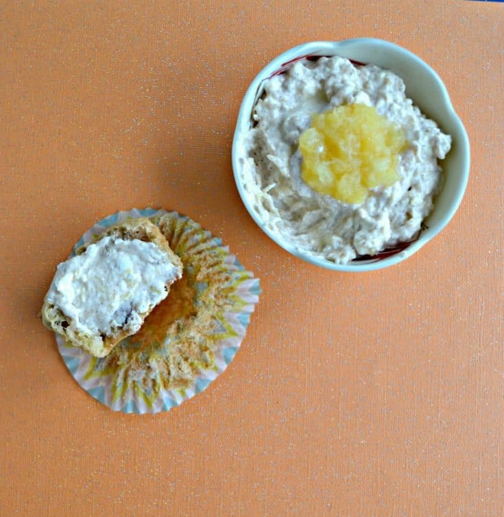 In the right upper corner is A bowl filled with cream cheese with a spoonful of rushed pineapple on top on an orange background then there is a half eaten muffin spread with the cream cheese on the lower left hand corner.