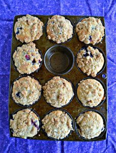 A muffin tin with 11 Sourdough Berry Muffins in it on a purple place mat.
