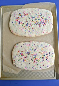 A sheet pan covered in parchment paper with two biscotti logs on top covered in sprinkles.