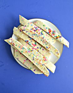 Blue background with a plate piled with rainbow sprinkle biscotti