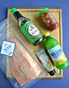 Ingredients for Korean Style BBQ Salmon on a cutting board: A large salmon filet, ssoy sauce, chile paste, ginger, lemon juice.