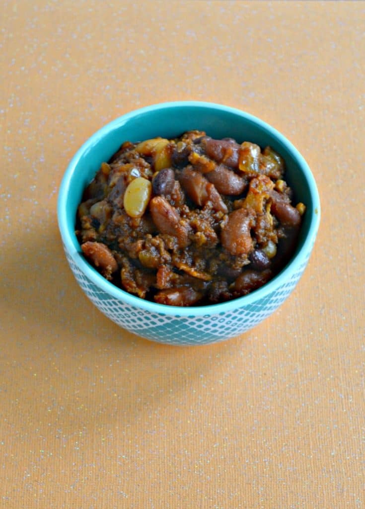 A blue bowl with a heaping mound of baked beans on an orange backdrop.