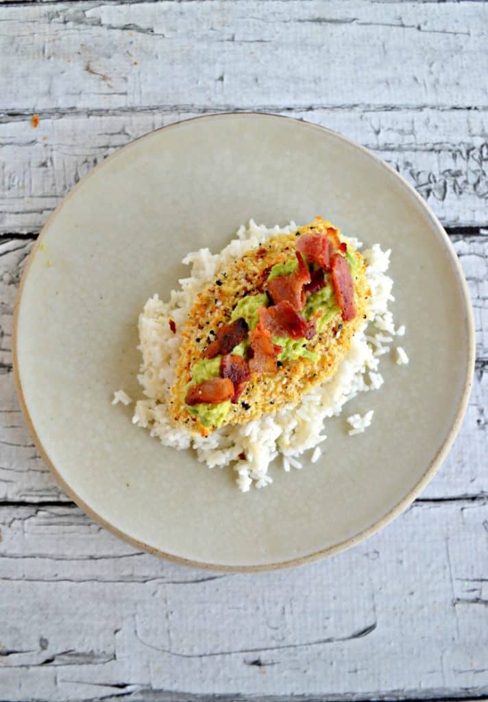 Plate topped with rice, breaded chicken, avocado, and bacon on a white background.