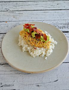 Side view of Plate topped with rice, breaded chicken, avocado, and bacon on a white background.