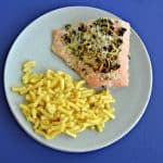 A plate with a large piece of salmon topped with herbs and a serving of macaroni and cheese with a blue background.