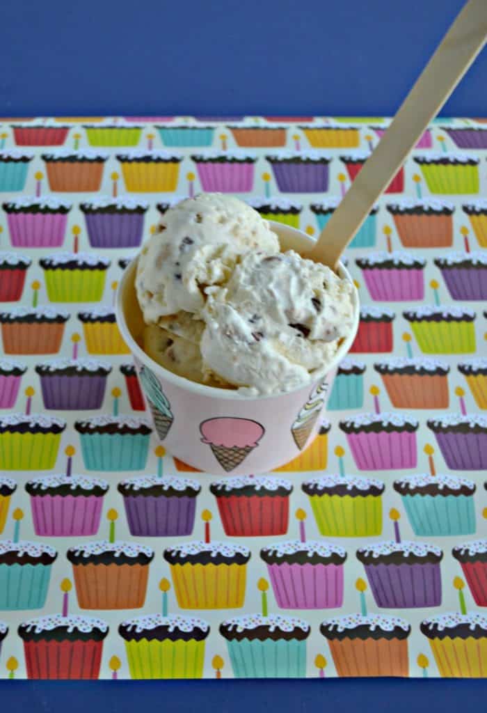 A cup of ice cream with 3 scoops and a wooden spoon on a cupcake background.