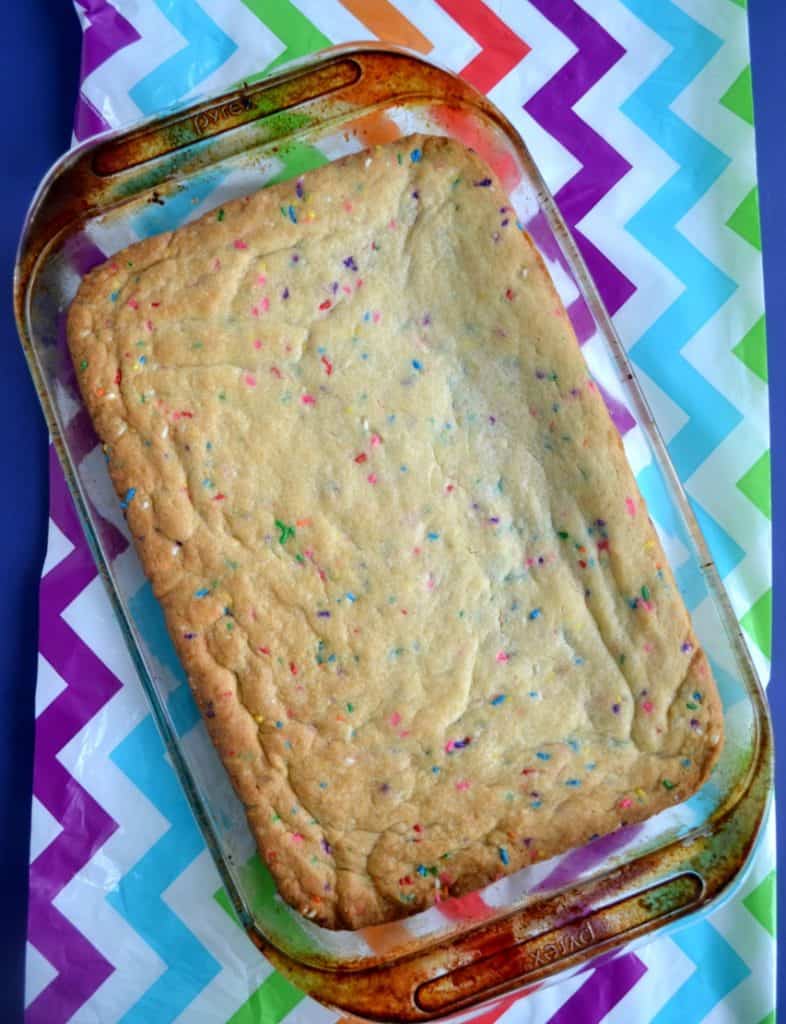 A pan of Funfetti cookie bars in a glass pan sitting on a rainbow tablecloth