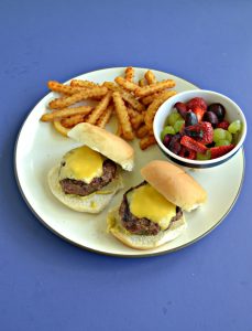 Top view of a plate with two burger sliders, a handful of fries, and a cup of mixed fruit on a blue background,