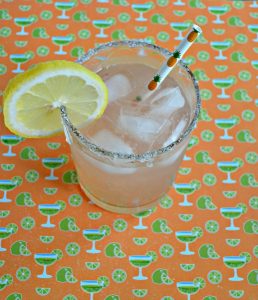 Top view of margarita in a glass with a straw and lemon on an orange and green margarita glass backdrop.