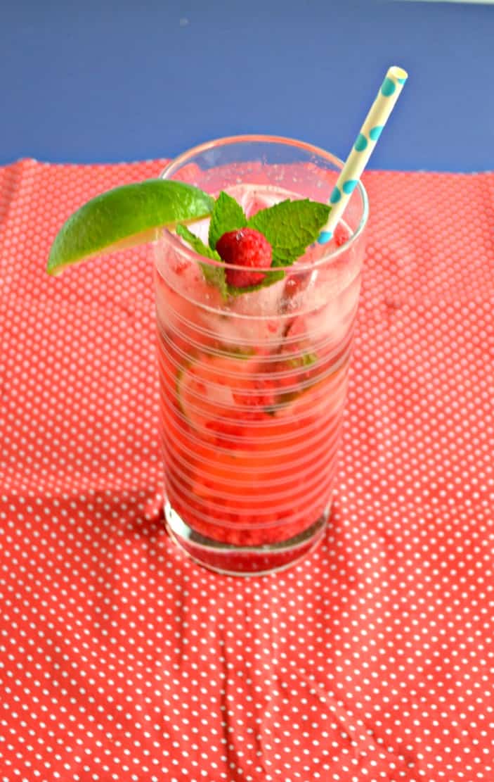 Raspberry Mojito in a tall glass garnished with a raspberry and mint sprig with a paper straw.
