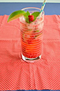 Raspberry Mojito in a tall glass filled with ice garnished with a raspberry and mint sprig with a paper straw.