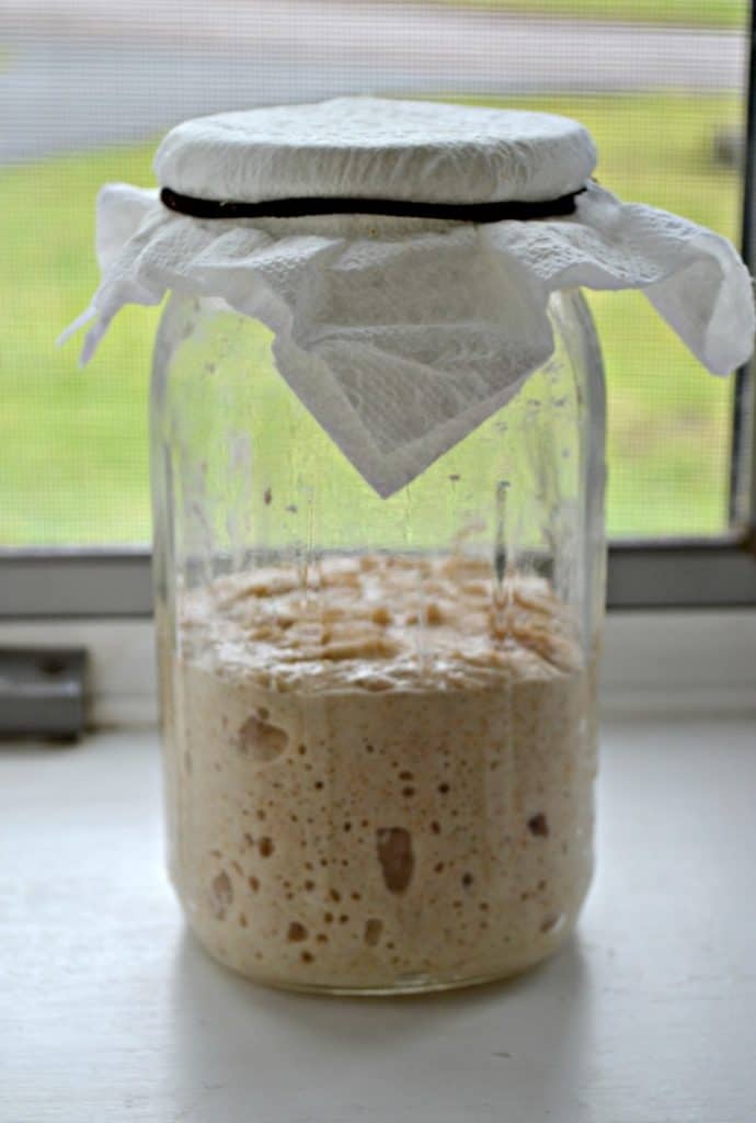 A jar topped with a napkin half full with a bubbling sourdough starter.