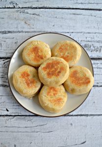 A white plate topped with 6 golden brown English Muffins
