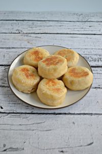 Side view of A white plate topped with 6 golden brown English Muffins