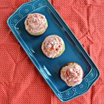 3 cupcakes topped with pink frosting sitting on a blue platter on a red backdrop.