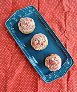 3 cupcakes topped with pink frosting sitting on a blue platter on a red backdrop.