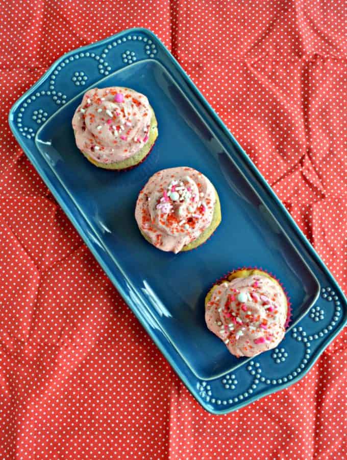 3 cupcakes topped with pink frosting sitting on a blue platter on a red backdrop.