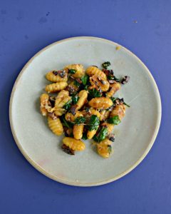 Top view of a plate with a pile of crispy gnocchi, wilted spinach, and cooked mushrooms.