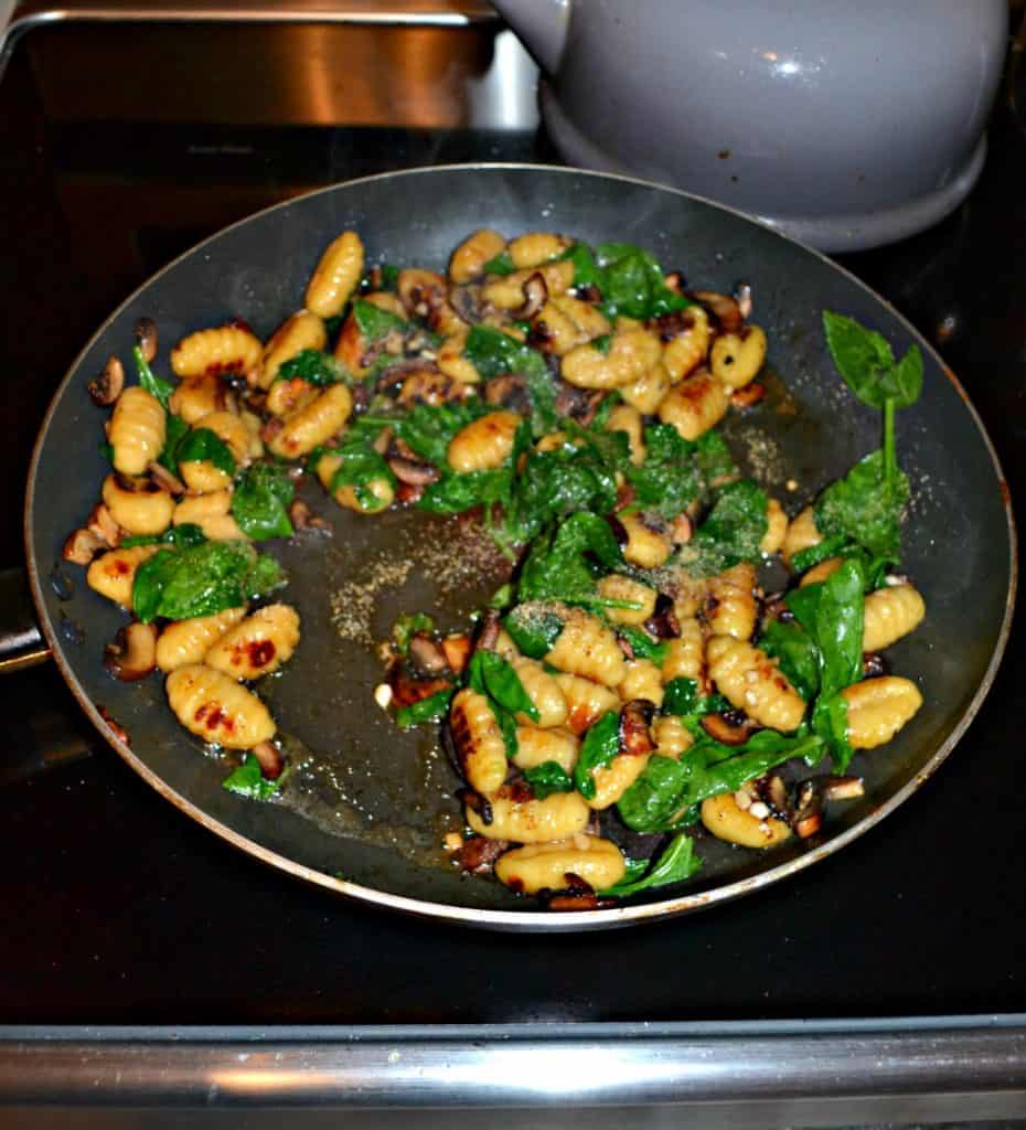 A saute pan with browned gnocchi, cooked mushrooms, and wilted spinach.