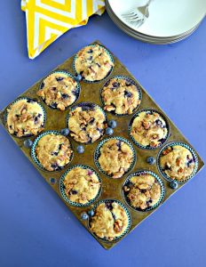 A muffin tin filled with blueberry muffins with a yellow napkin peeking in from the top.