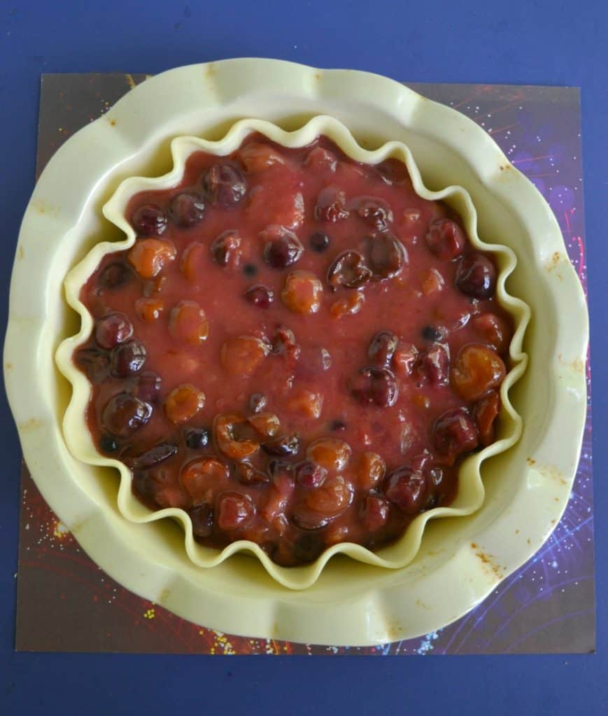 A pie pan with an unbaked fluted crust filled with red and purple berries and rhubarb.
