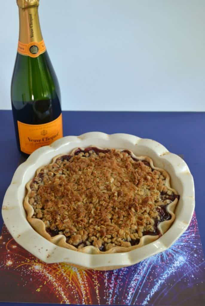 A pie pan filled with a baked pie and golden brown crumble top with a green champagne bottle in the background.
