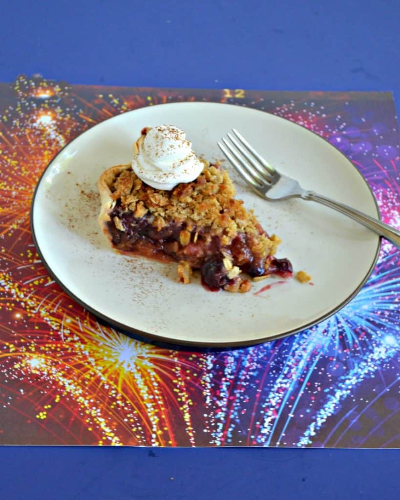 A plate topped with a slice of pie with a scoop of whipped cream on top with a fork sitting next to it sitting on a firework background.