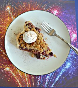 A top view of a plate topped with a slice of pie with a scoop of whipped cream on top with a fork sitting next to it sitting on a firework background.