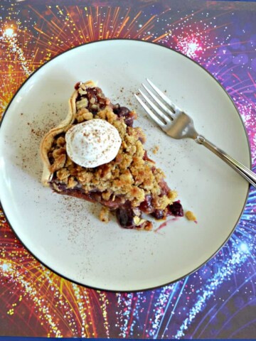 A top view of a plate topped with a slice of pie with a scoop of whipped cream on top with a fork sitting next to it sitting on a firework background.