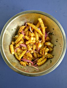 A silver bowl filled with crinkle fries and red onions on a blue background.