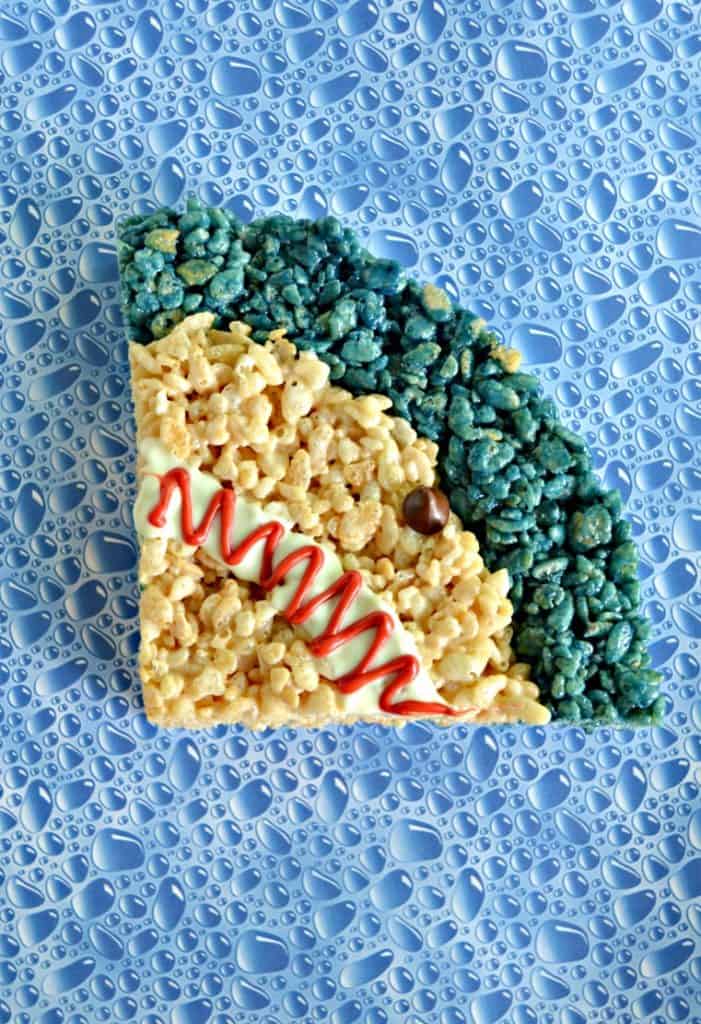Blue bubble background with a shark rice krispie treat on it (A quarter of a circle with a small blue stripe at the top, regular rice krispies for the rest, a white mouth with red squiggle, and a chocolate chip eye.