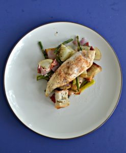 A plate piled with asparagus, potatoes, and a chicken breast on top on a blue background.