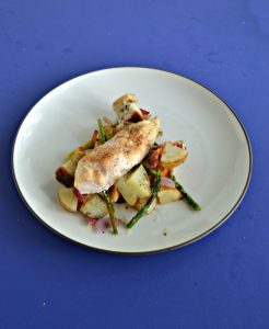 A plate topped with potatoes and asparagus with a chicken breast on top on a blue background.