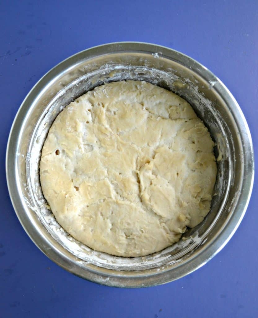 A bowl filled with sourdough pizza dough on a blue background.