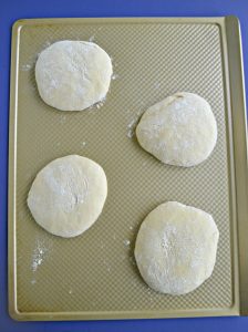 A cookie sheet with four mounds of pizza dough on it.